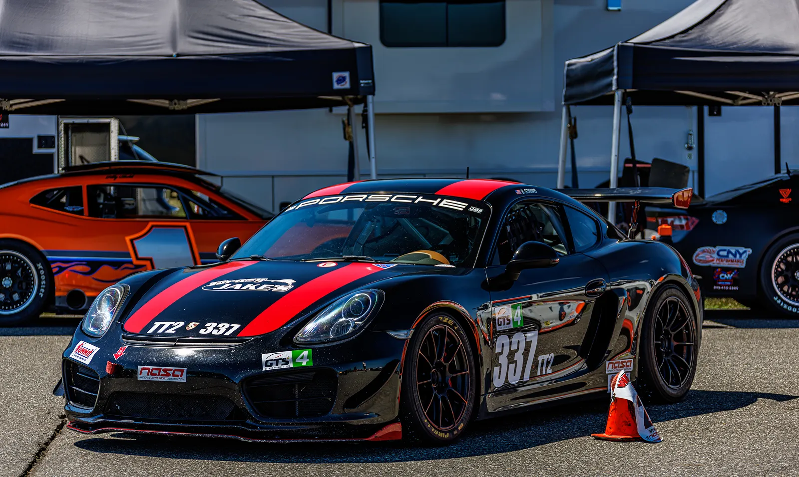 GT4 race car parked in front of a building, with a traffic cone on the road